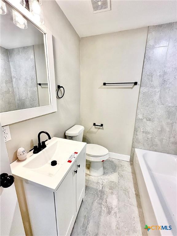 bathroom featuring toilet, a washtub, and vanity