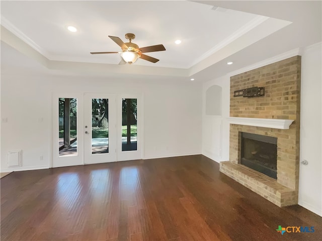 unfurnished living room with ornamental molding, ceiling fan, dark hardwood / wood-style floors, a raised ceiling, and a brick fireplace