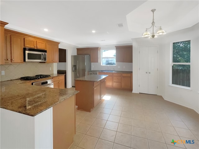 kitchen with a kitchen island, appliances with stainless steel finishes, pendant lighting, sink, and a chandelier