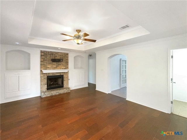 unfurnished living room featuring dark wood-type flooring, a tray ceiling, ceiling fan, and a fireplace