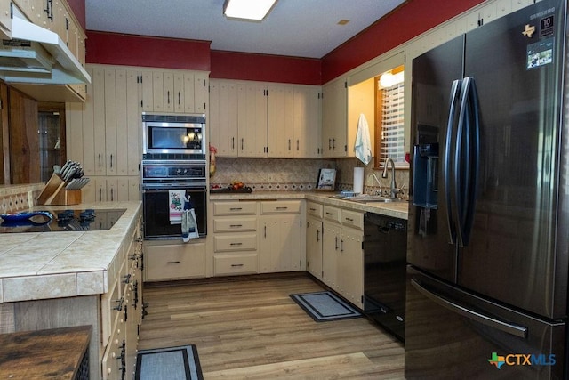 3309 Cottonwood Ln, Temple, TX 76502 - kitchen featuring black appliances, under cabinet range hood, tile counters, light wood finished floors, and decorative backsplash
