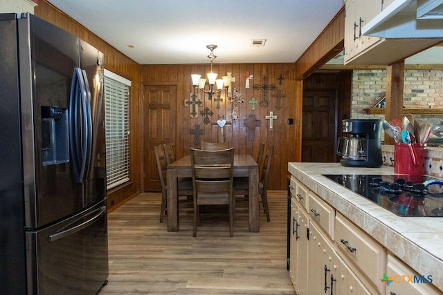 3309 Cottonwood Ln, Temple, TX 76502 - kitchen featuring stainless steel fridge, tile countertops, black electric stovetop, a chandelier, and wood walls