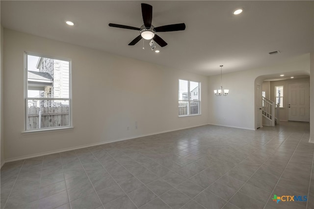 tiled spare room featuring ceiling fan with notable chandelier