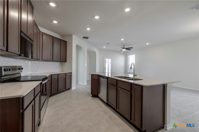 kitchen with sink, an island with sink, tasteful backsplash, dark brown cabinetry, and stainless steel appliances