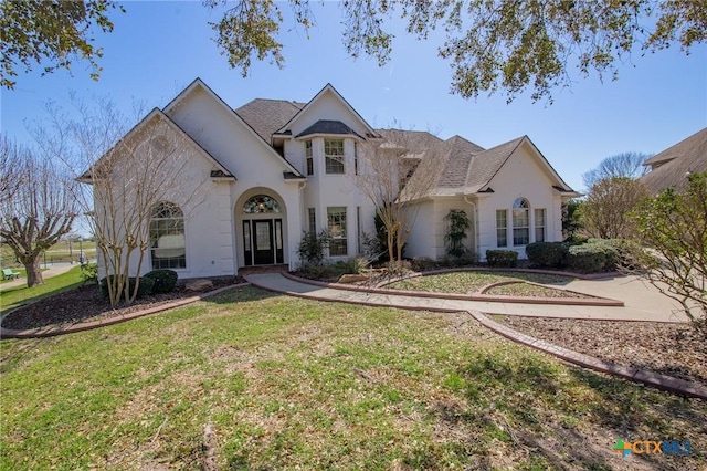 french country inspired facade featuring stucco siding, a front lawn, and roof with shingles