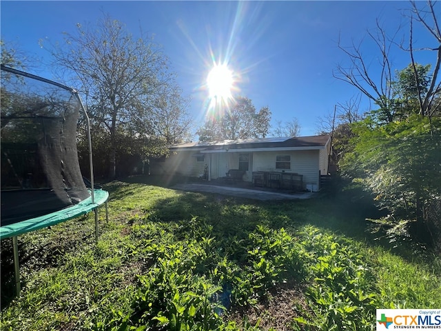 rear view of property with a trampoline, a lawn, and a patio area