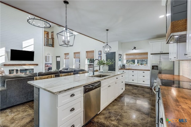 kitchen with butcher block counters, sink, an island with sink, appliances with stainless steel finishes, and white cabinetry