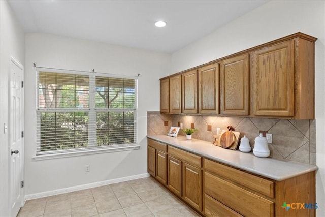 7778 Little Deer Trl, Georgetown, TX 78628 - kitchen with brown cabinetry, baseboards, light tile patterned flooring, decorative backsplash, and light countertops