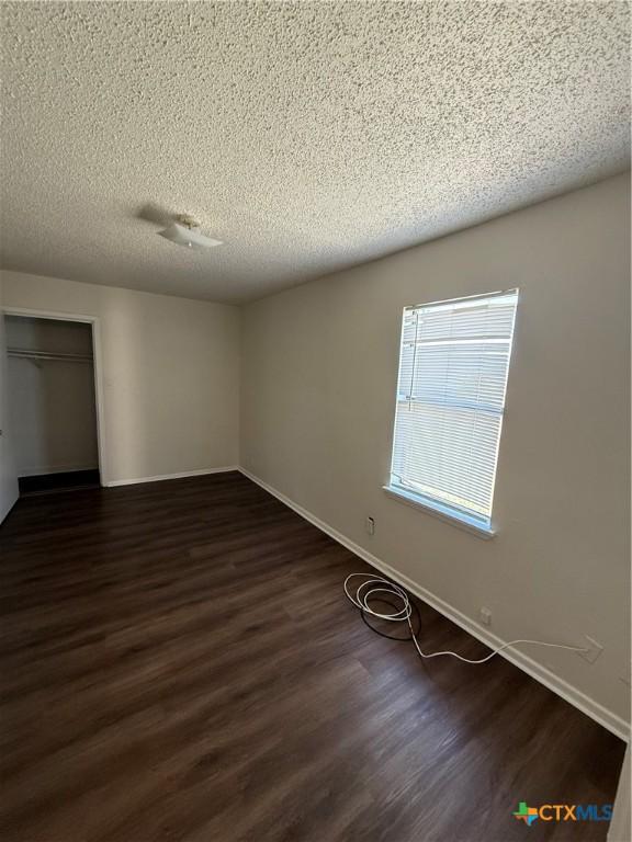 unfurnished room featuring a textured ceiling, dark wood-type flooring, and baseboards