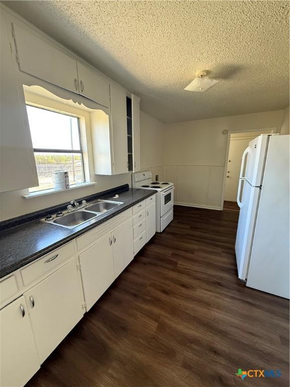 kitchen featuring dark countertops, white appliances, white cabinetry, and a sink