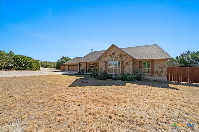 view of front facade with a garage, stone siding, and fence