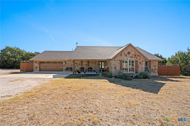 view of front of house with a garage, stone siding, fence, and driveway