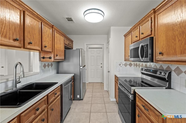 kitchen with sink, a textured ceiling, light tile patterned floors, stainless steel appliances, and decorative backsplash