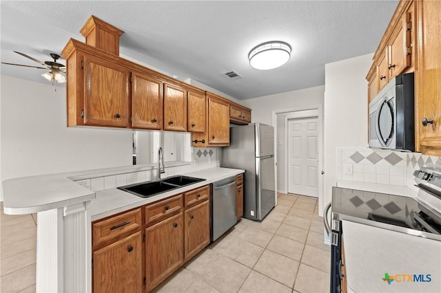 kitchen with sink, a textured ceiling, light tile patterned floors, appliances with stainless steel finishes, and kitchen peninsula