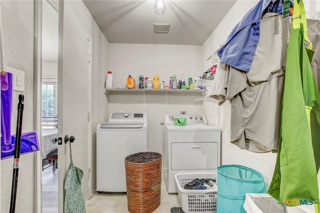 washroom with a textured ceiling, visible vents, washer and dryer, laundry area, and light tile patterned floors