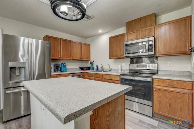 kitchen featuring light countertops, a sink, light wood-type flooring, brown cabinetry, and appliances with stainless steel finishes