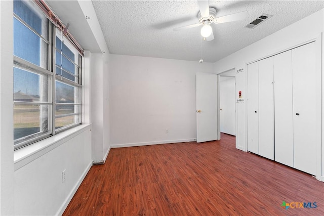 unfurnished bedroom featuring wood finished floors, baseboards, visible vents, a closet, and a textured ceiling