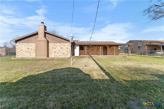 back of property with brick siding, a lawn, a chimney, and fence