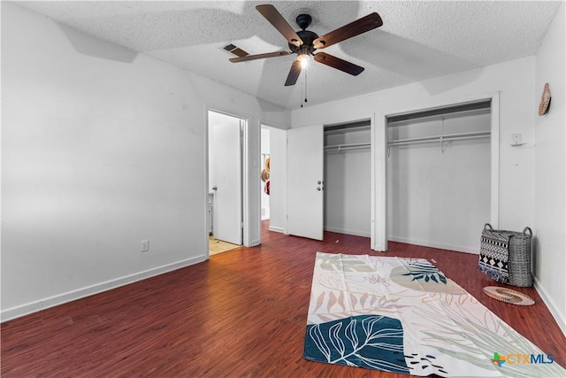 bedroom featuring a textured ceiling, two closets, baseboards, and wood finished floors