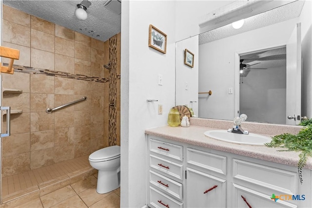 bathroom featuring vanity, a tile shower, ceiling fan, a textured ceiling, and toilet