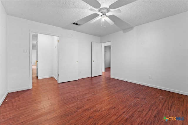 unfurnished bedroom featuring visible vents, a textured ceiling, baseboards, and wood finished floors