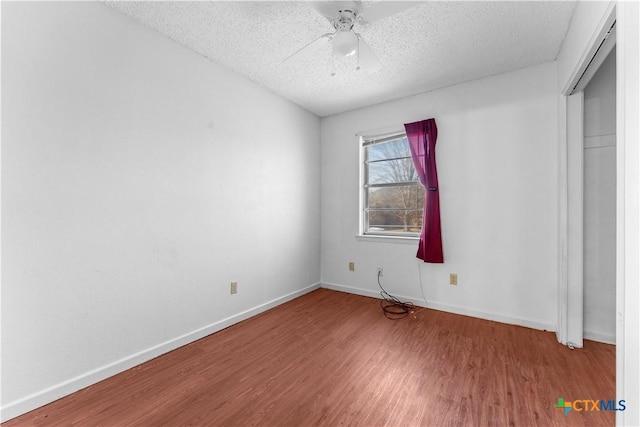 unfurnished bedroom featuring a textured ceiling, a ceiling fan, baseboards, and wood finished floors