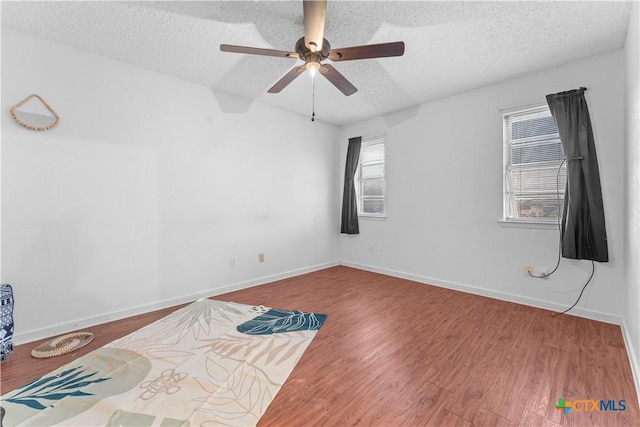 empty room featuring baseboards, a textured ceiling, a ceiling fan, and wood finished floors