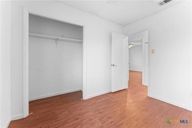 unfurnished bedroom featuring wood finished floors, visible vents, a closet, and baseboards