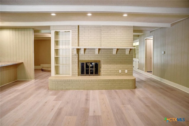 1705 Neuman St, Gonzales, TX 78629 - unfurnished living room with light wood finished floors, a brick fireplace, beam ceiling, and wooden walls