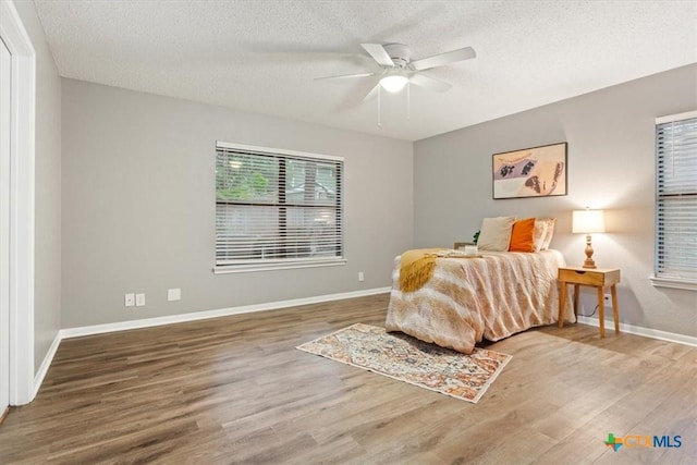 bedroom featuring wood finished floors, a textured ceiling, baseboards, and a ceiling fan
