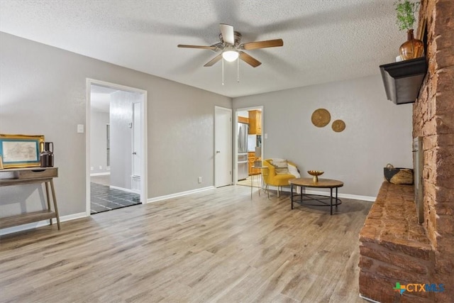 living area featuring ceiling fan, wood finished floors, a textured ceiling, and baseboards