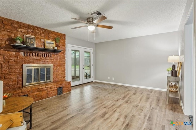 unfurnished living room featuring wood finished floors, ceiling fan, a textured ceiling, baseboards, and a brick fireplace
