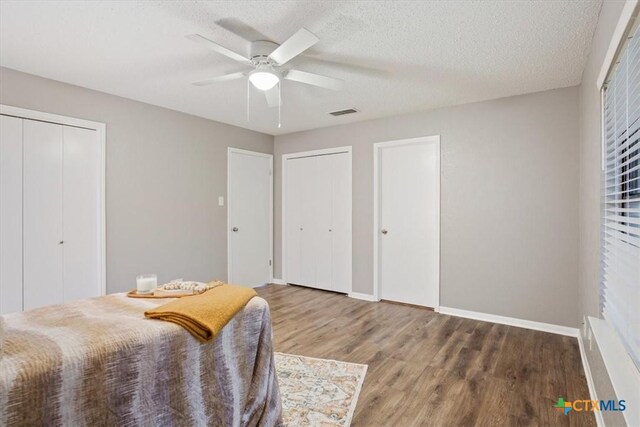 bedroom featuring two closets, wood finished floors, baseboards, a ceiling fan, and a textured ceiling