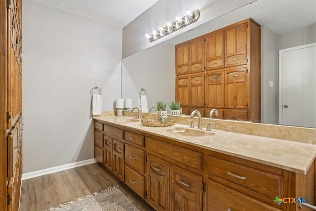 full bathroom with a textured ceiling, wood finished floors, baseboards, and double vanity