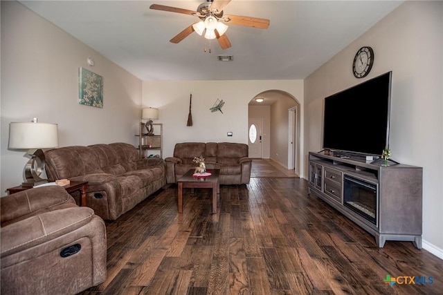 living room featuring arched walkways, dark wood-style flooring, visible vents, a ceiling fan, and baseboards