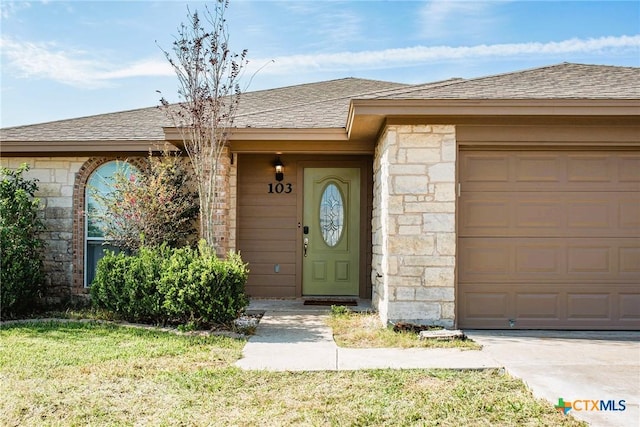 property entrance featuring a garage, stone siding, a yard, and roof with shingles