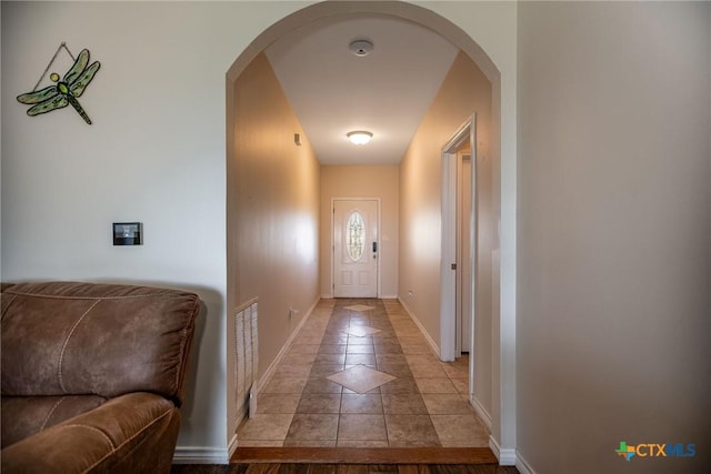 entryway featuring arched walkways, light tile patterned floors, and baseboards