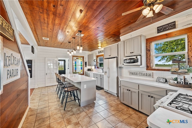 kitchen with pendant lighting, a wealth of natural light, wooden walls, and white appliances