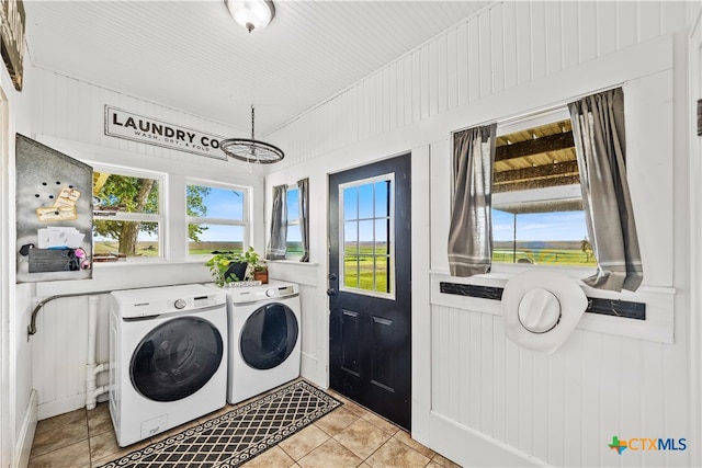 laundry room featuring plenty of natural light, wooden walls, light tile patterned floors, and washing machine and clothes dryer