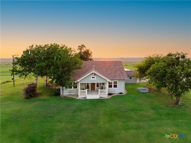 back house at dusk with a porch and a yard