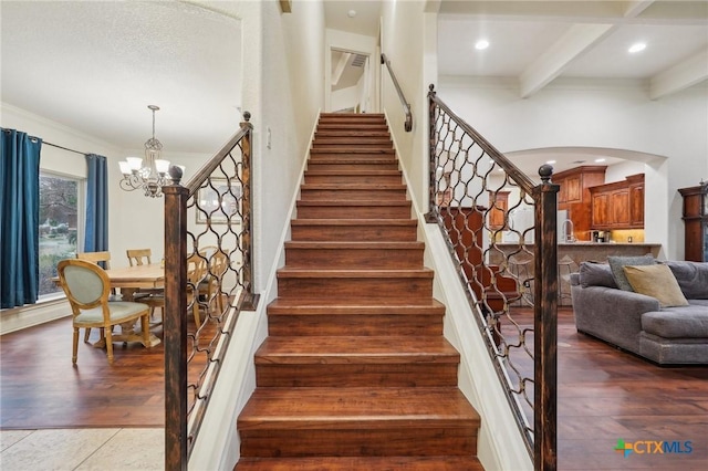 stairway featuring hardwood / wood-style floors, ornamental molding, a notable chandelier, and beam ceiling