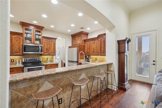 kitchen featuring stacked washing maching and dryer, appliances with stainless steel finishes, a kitchen bar, and backsplash