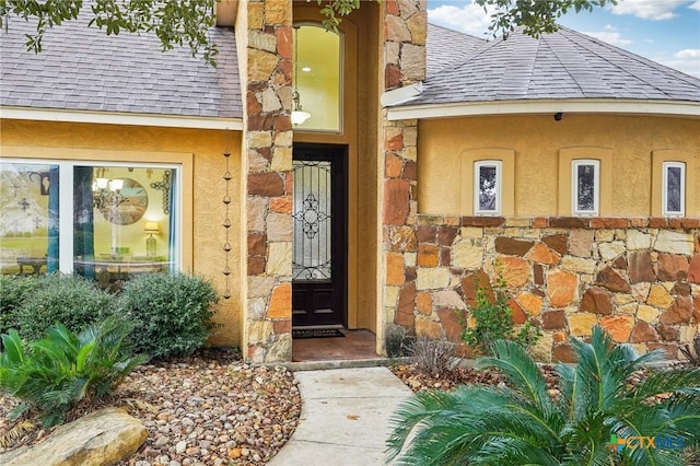 entrance to property featuring stone siding, stucco siding, and a shingled roof