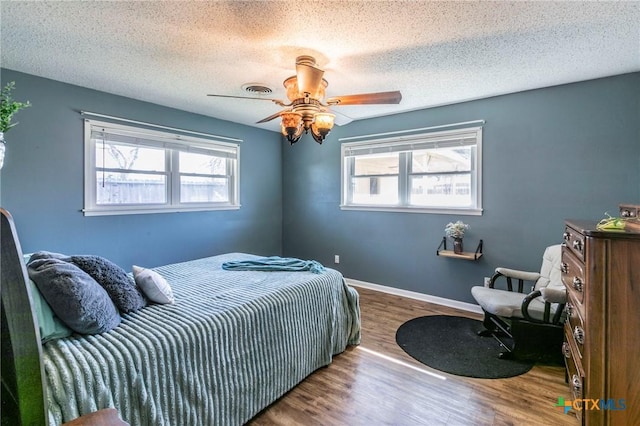 bedroom featuring multiple windows, hardwood / wood-style floors, a textured ceiling, and ceiling fan