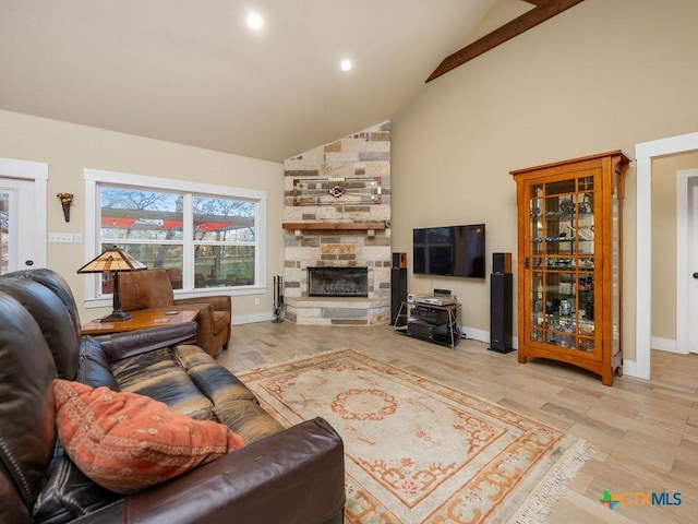 living area with high vaulted ceiling, a stone fireplace, and light wood-style flooring