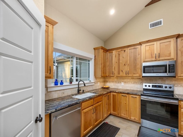 kitchen with lofted ceiling, a sink, visible vents, appliances with stainless steel finishes, and dark stone countertops