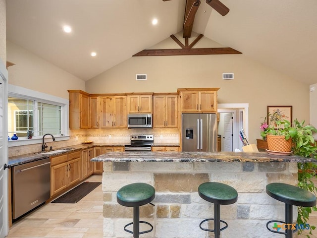 kitchen featuring dark stone counters, stainless steel appliances, a kitchen bar, and a sink