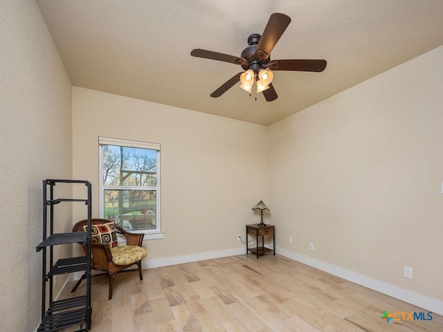 sitting room with light wood-type flooring, ceiling fan, baseboards, and a textured ceiling