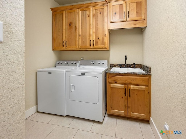 clothes washing area with light tile patterned floors, cabinet space, a sink, washer and dryer, and baseboards