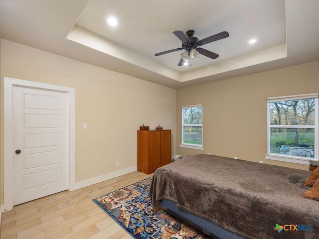 bedroom featuring light wood-style floors, a tray ceiling, baseboards, and recessed lighting